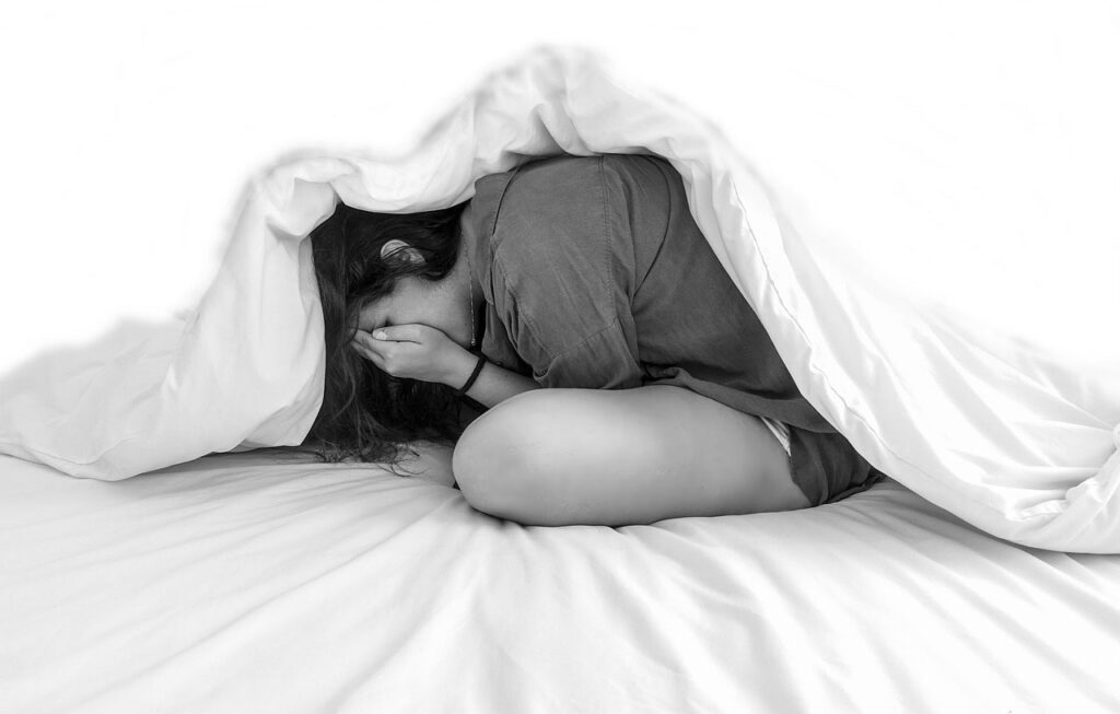 Teenage girl with anxiety hiding under blanket
